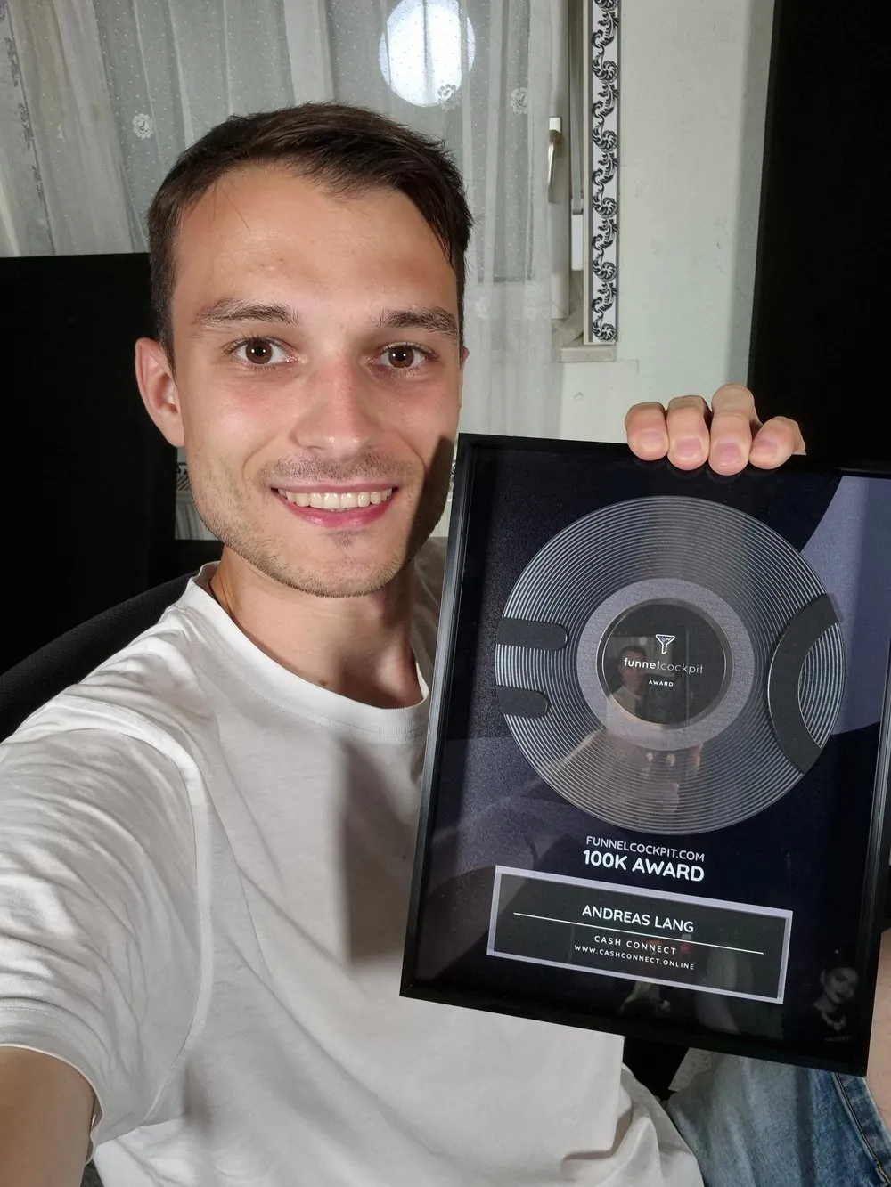 Andreas Lang lächelt in die Kamera und hält eine gerahmte Auszeichnung mit der Aufschrift 100K Award