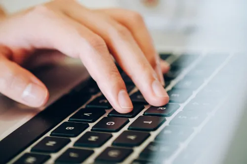 Nahaufnahme einer Hand, die auf der Tastatur eines Laptops tippt