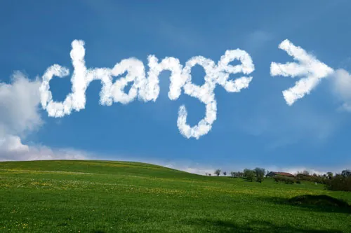 Das Wort change als Wolkenschrift mit Pfeil am blauen Himmel über einer grünen Wiese