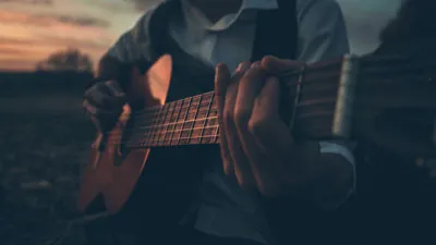Nahaufnahme einer Hand, die im Abendlicht auf einer akustischen Gitarre spielt