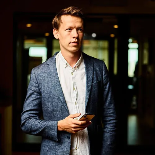 Porträt von Alexander Heeg im Sakko mit Smartphone in der Hand