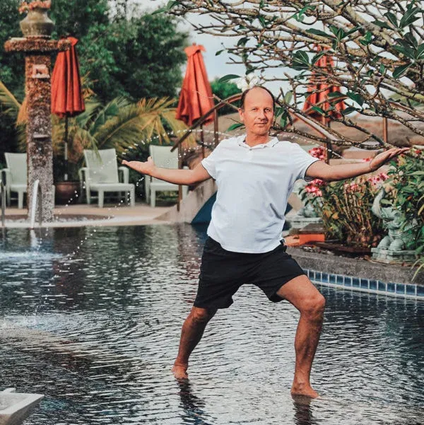Remo Rittiner in einer Yogahaltung barfuß im flachen Wasser eines Pools, im Hintergrund Palmen und Sonnenschirme