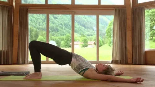 Frau in der Brücke, einer Rückbeuge, auf einer Matte in einem Holzsaal mit großen Fenstern