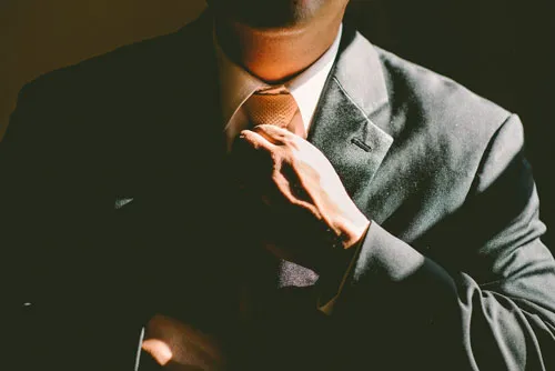 Mann im Anzug richtet seine Krawatte – Symbolbild zum Business Master Kurs
