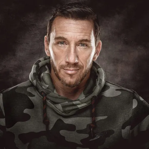 Porträt von Calvin Hollywood im Camouflage-Hoodie vor dunklem Hintergrund