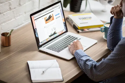 Person arbeitet am Laptop an einem Schreibtisch mit Notizbuch und Startup-Buch