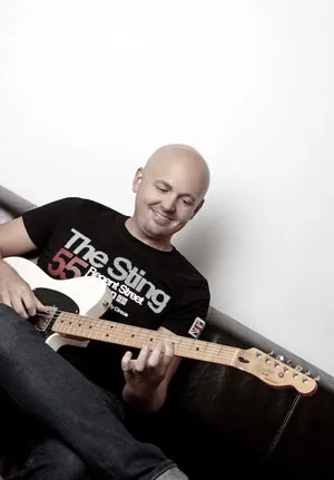 Gitarrist Christian Konrad sitzt mit einer E-Gitarre an einer weißen Wand