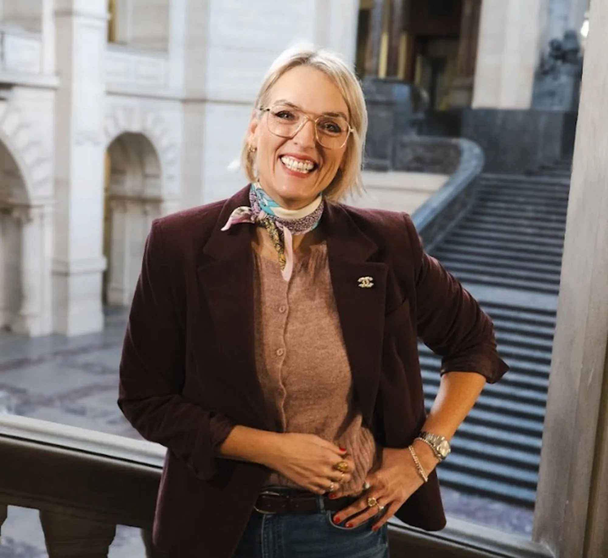 Claudia Albers im weinroten Samtblazer mit Seidentuch in einem historischen Treppenhaus