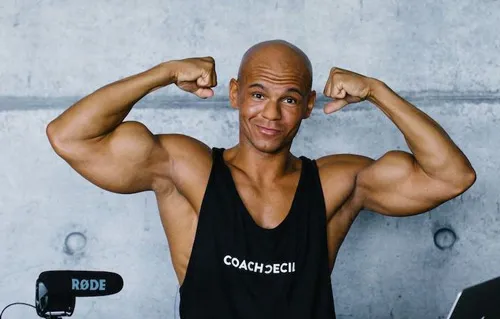 Coach Cecil im schwarzen Coach-Cecil-Tanktop spannt beide Bizepse an