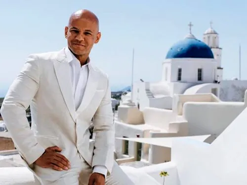 Coach Cecil im weißen Anzug vor einer Kirche mit blauer Kuppel auf Santorini