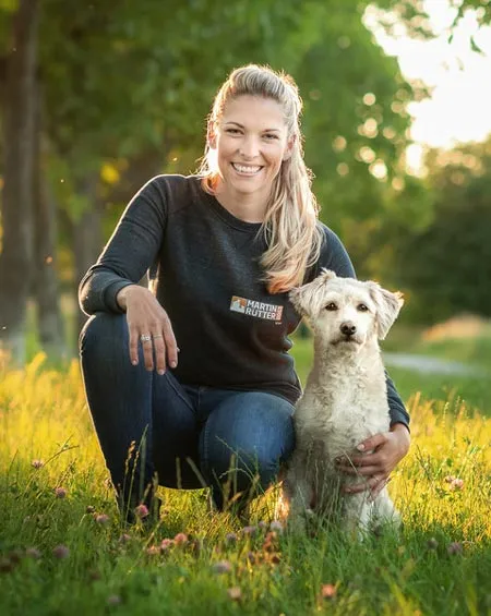 Hunde-Trainerin Conny Sporrer kniet mit einem weißen Hund auf einer sonnigen Wiese