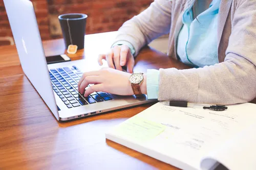Frau schreibt am Laptop auf einem Holztisch neben Notizen und Kaffeebecher – Copywriting umsetzen