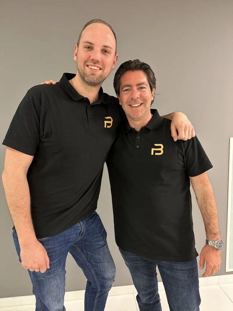 Fabian Habich und Daniel Kocks in schwarzen Poloshirts mit dem Logo von Profit Buddies vor einer grauen Wand