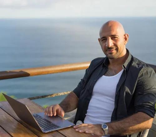 Darek Shabany sitzt mit Laptop an einem Tisch am Meer