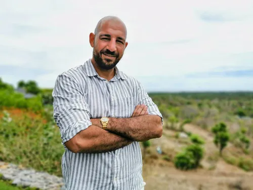 Darek Shabany mit verschränkten Armen im gestreiften Hemd vor einer grünen Landschaft