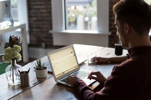 Mann arbeitet an einem Holztisch am Laptop am perfekten Laptop Business