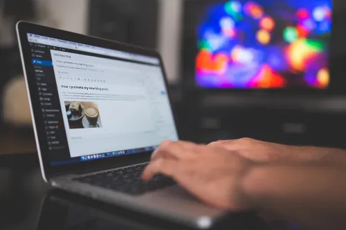Hände tippen auf einem Laptop mit geöffnetem Blog-Editor vor bunt leuchtendem Hintergrund