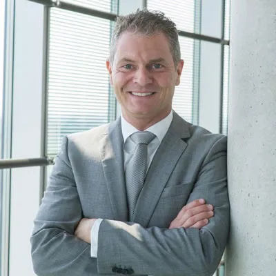 Dirk Kreuter im grauen Anzug mit verschränkten Armen vor einer Fensterfront