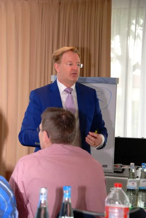 Dirk-Michael Lambert im blauen Anzug hält vor Teilnehmern einen Vortrag am Flipchart