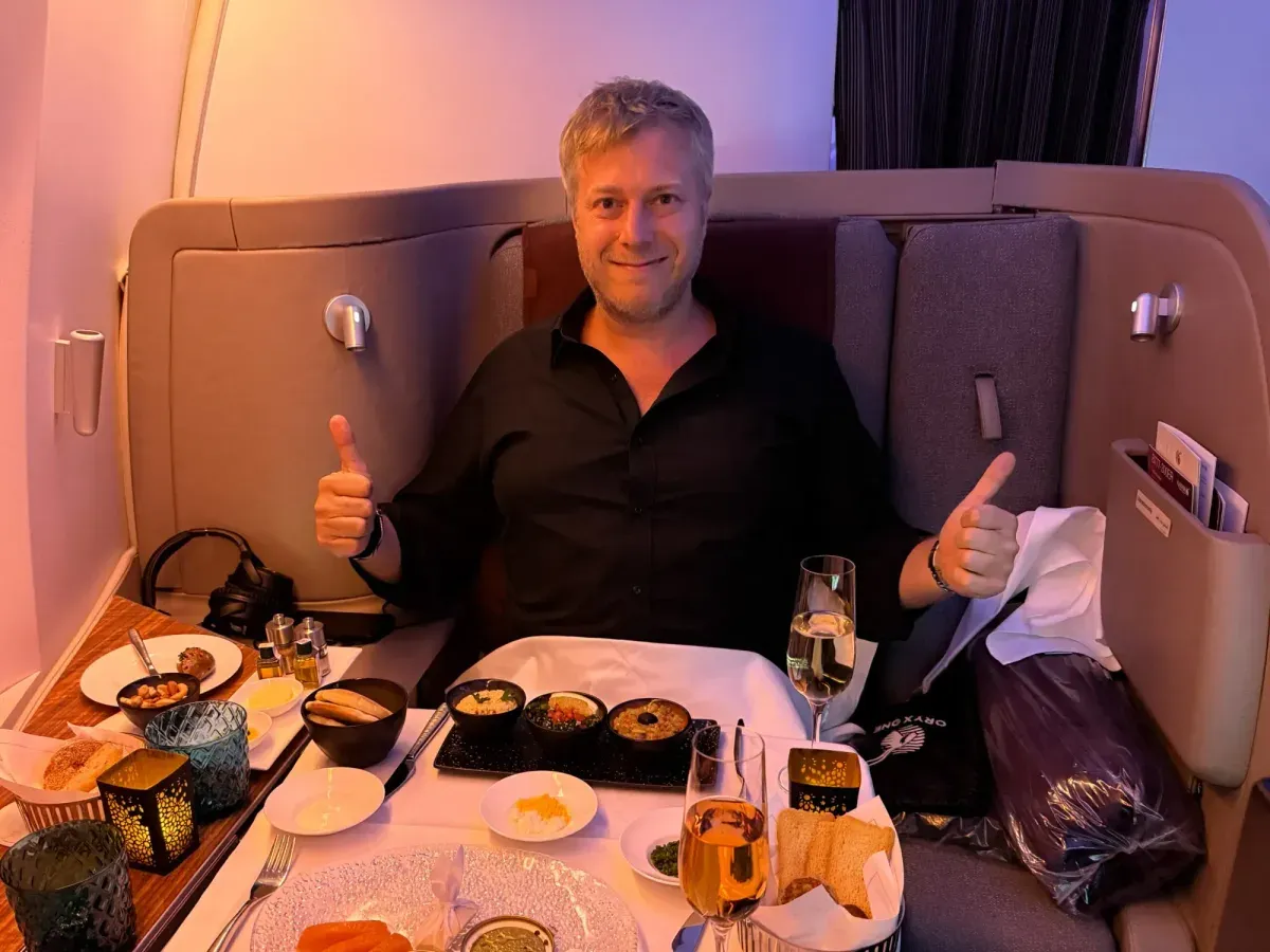 Fabian Hilpert mit erhobenen Daumen an einem gedeckten Tisch in einer Flugzeugkabine der First Class