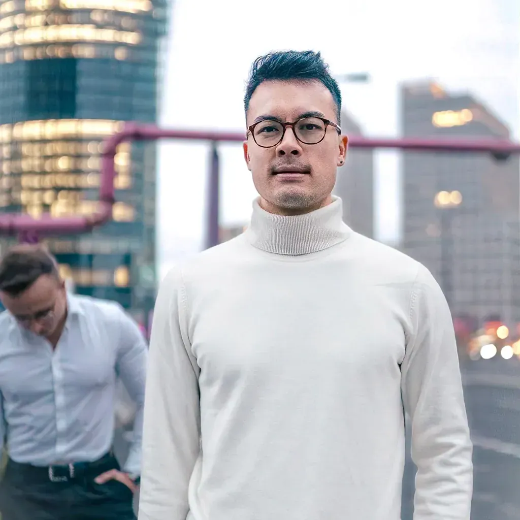 Erik Pfeiffer mit Brille und hellem Rollkragenpullover vor einer Stadtkulisse
