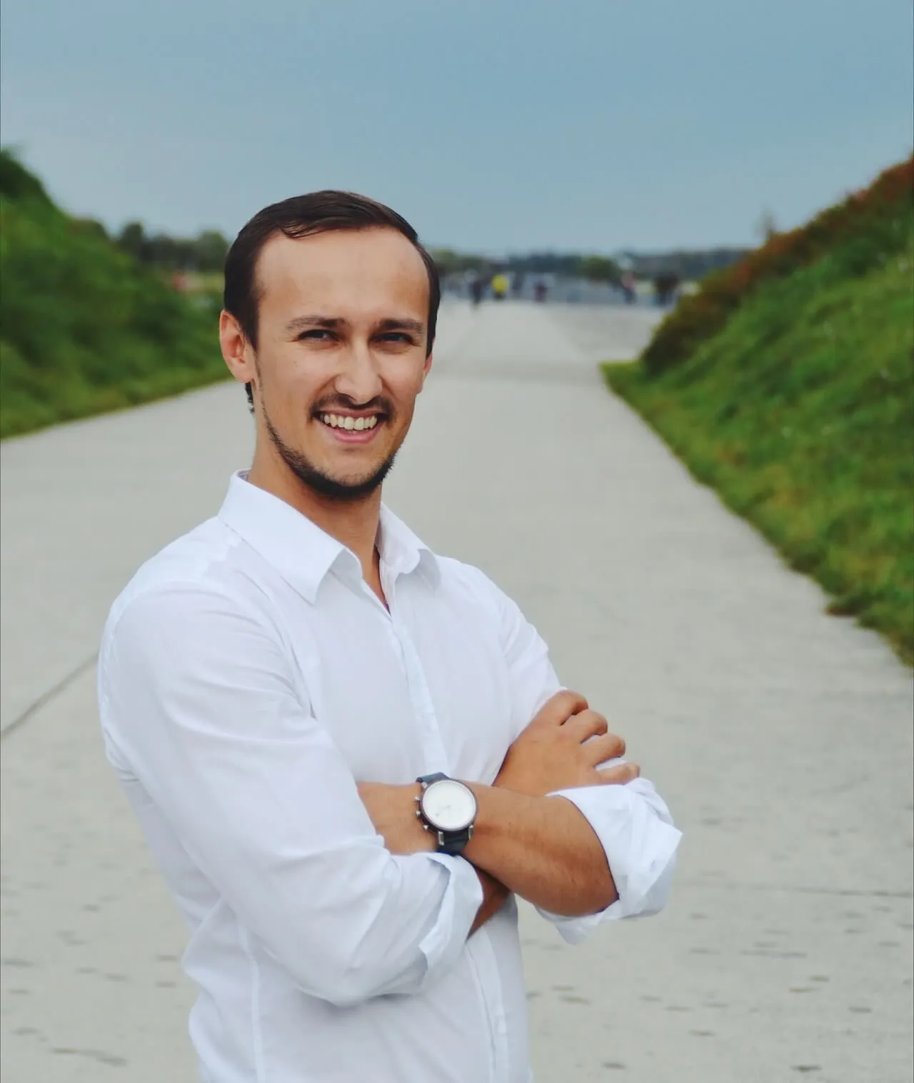 Eugen Grinschuk im weißen Hemd mit verschränkten Armen, lachend auf einem Weg zwischen grünen Böschungen