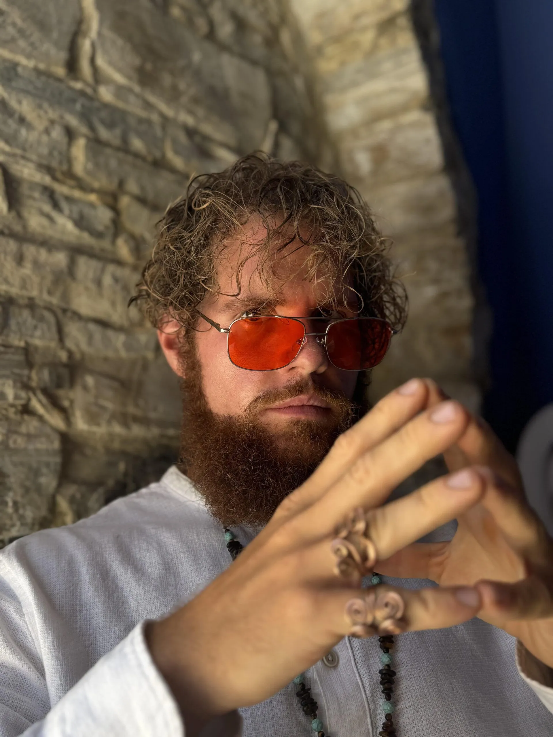 Fabian Kowallik mit Locken, Bart und roter Sonnenbrille vor einer Steinwand
