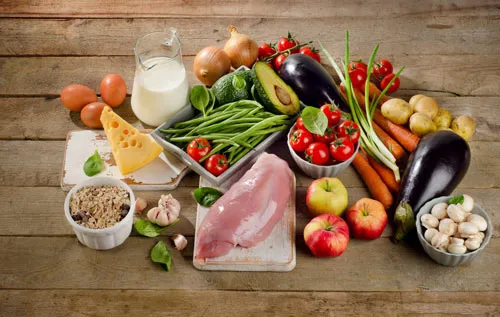 Frische Lebensmittel wie Gemüse, Obst, Fleisch, Käse und Milch auf einem Holztisch zum Modul Ernährung
