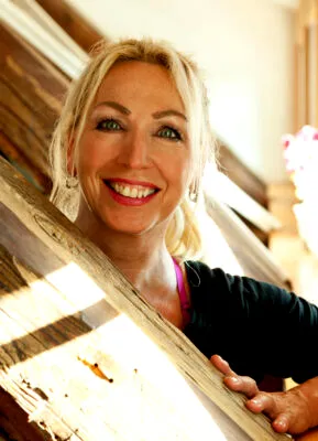Porträt der lächelnden Pilates-Expertin Gabriela Höper an einem hölzernen Fensterrahmen