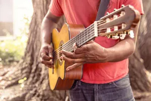 Mann im roten T-Shirt greift Akkorde auf einer akustischen Gitarre