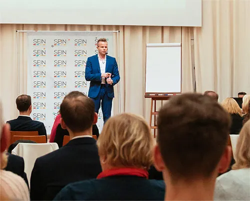 Gunnar Kessler im blauen Anzug spricht vor Publikum auf einem Seminar