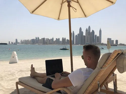 Gunnar Kessler arbeitet auf einer Strandliege mit Laptop vor der Skyline von Dubai