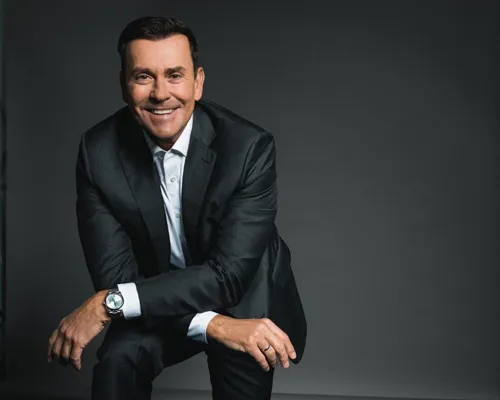 Jürgen Höller im dunklen Anzug sitzend vor grauem Hintergrund