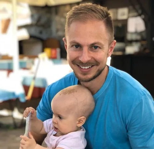 Juro Rajkovaca im blauen T-Shirt mit seinem Baby auf dem Arm