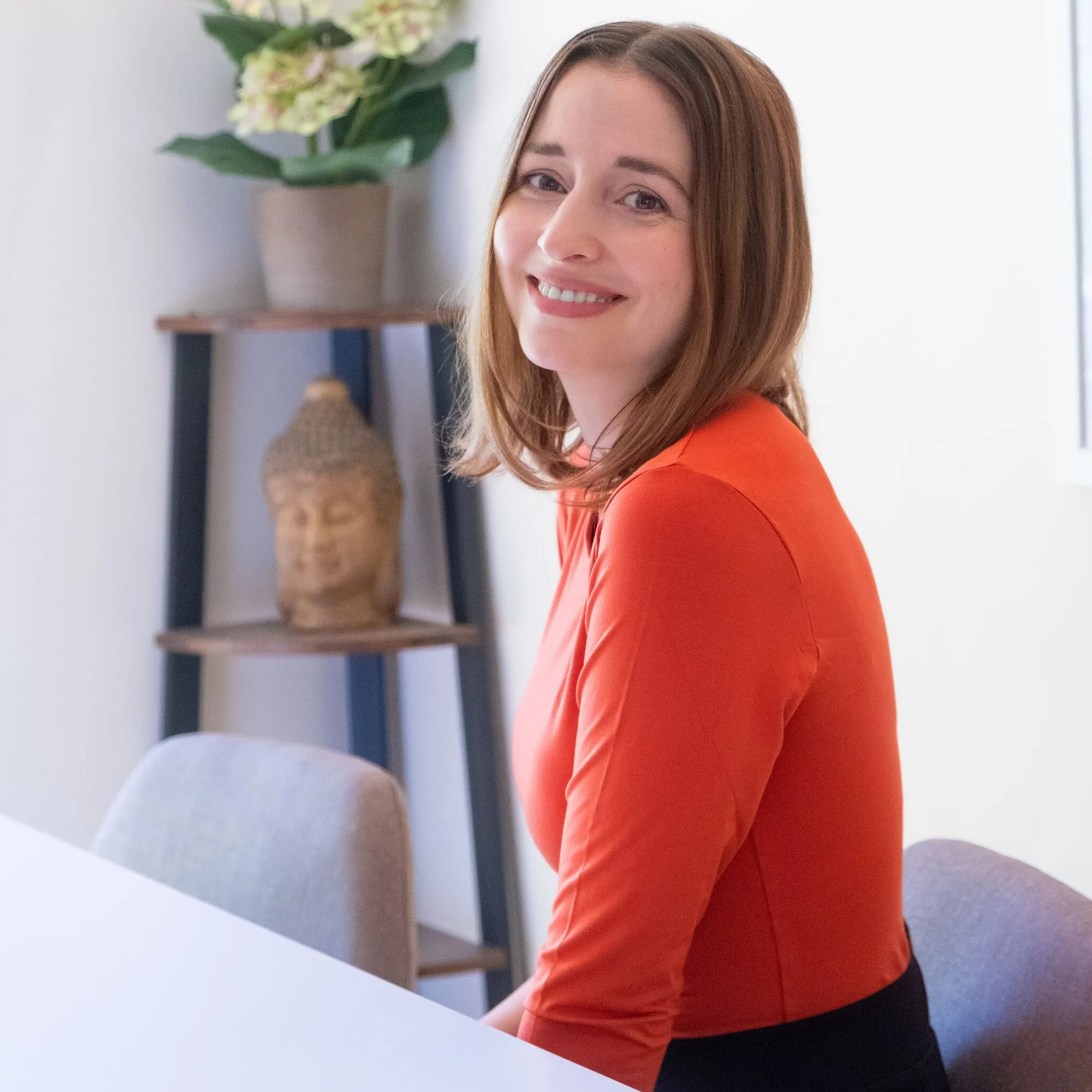 Dr. Katharina Tempel lächelnd im orangefarbenen Oberteil an einem hellen Tisch