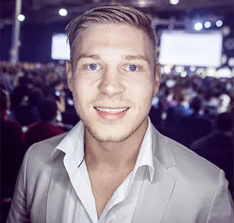 Porträt von Kris Stelljes im hellen Sakko vor einem Publikum auf einer Veranstaltung
