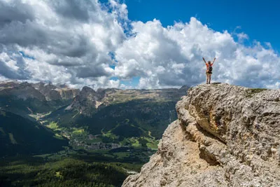 Person steht mit erhobenen Armen auf einem Felsen über einem Bergtal – Symbolbild für das nächste Level im Lebensstarter-System