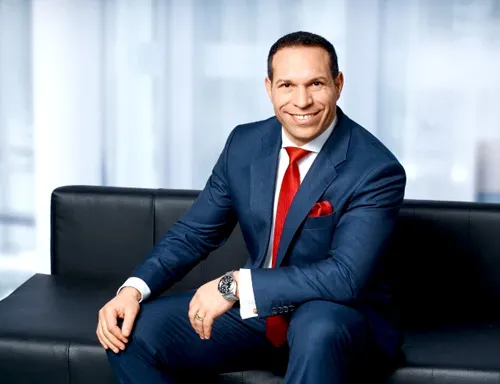 Marc Galal im dunkelblauen Anzug mit roter Krawatte auf einem schwarzen Ledersofa