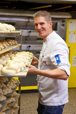 Marcel Paa in Bäckerkleidung vor einem Wagen mit frischen Backwaren in der Backstube