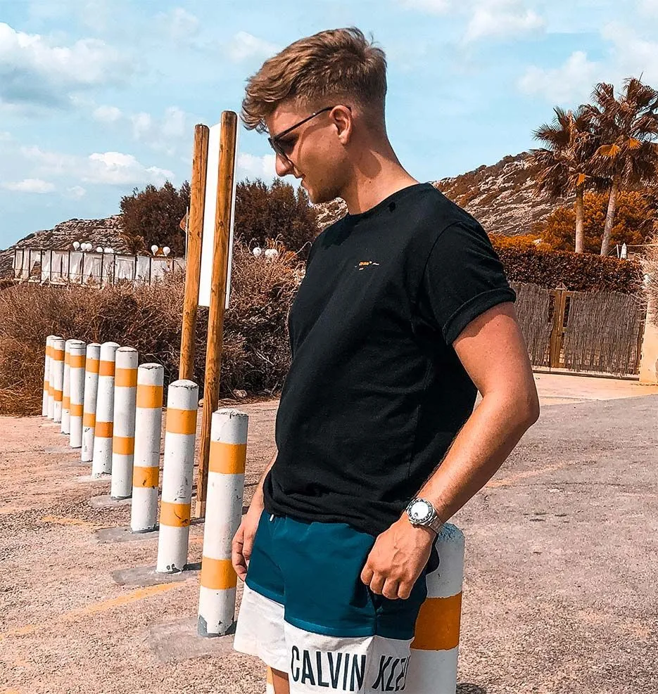 Marek Rühl mit Sonnenbrille und schwarzem T-Shirt vor Palmen
