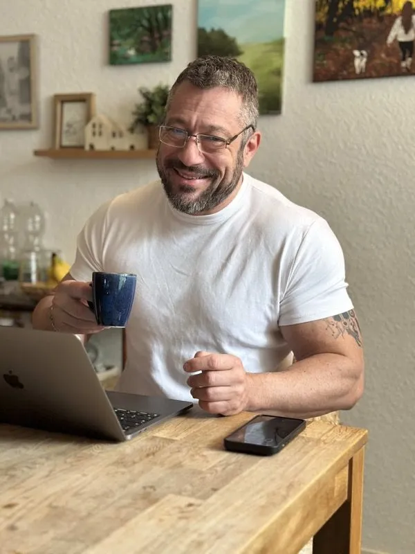 Mario Burgard lächelnd mit Kaffeetasse am Laptop