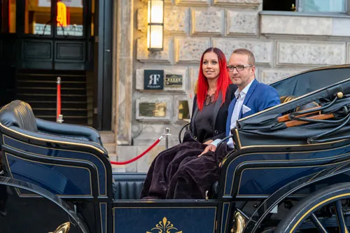 Marko und Mandy Slusarek sitzen in einer Pferdekutsche vor einem Hotel