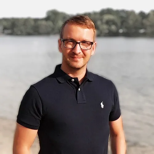 Marko Slusarek mit Brille im schwarzen Poloshirt vor einem See