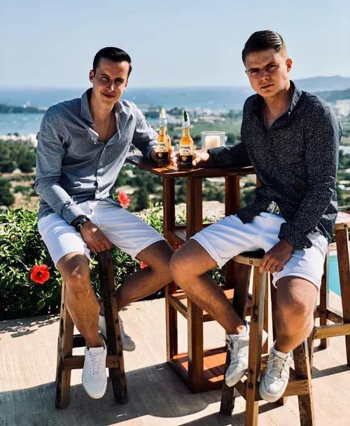Max und Max sitzen auf Barhockern an einem Tisch vor dem Meer
