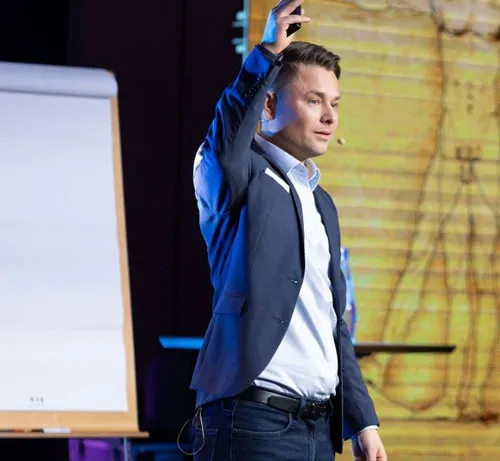Maxim Mankevich spricht mit erhobener Hand bei einem Vortrag auf der Bühne