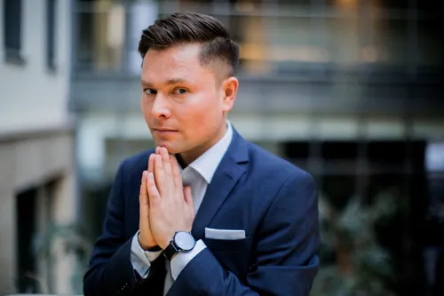 Maxim Mankevich im Anzug mit zusammengelegten Händen vor einem Gebäude