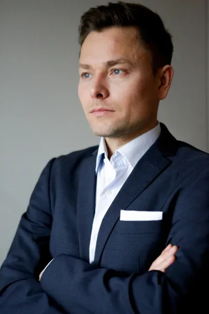 Maxim Mankevich im dunkelblauen Anzug mit verschränkten Armen vor hellem Hintergrund