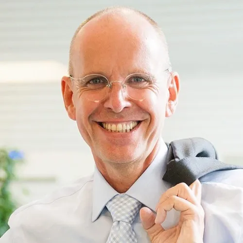 Porträt des lächelnden Verkaufstrainers Mike Dierssen mit Brille und Sakko über der Schulter