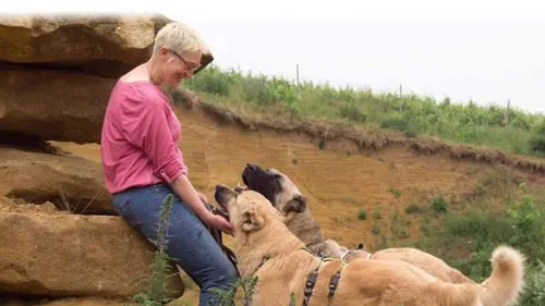 Mirjam Cordt sitzt auf einem Felsen und streichelt zwei Herdenschutzhunde