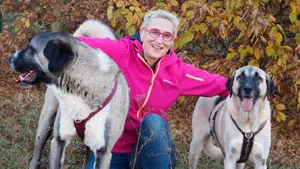 Mirjam Cordt kniet lachend zwischen zwei großen Herdenschutzhunden im Herbstlaub
